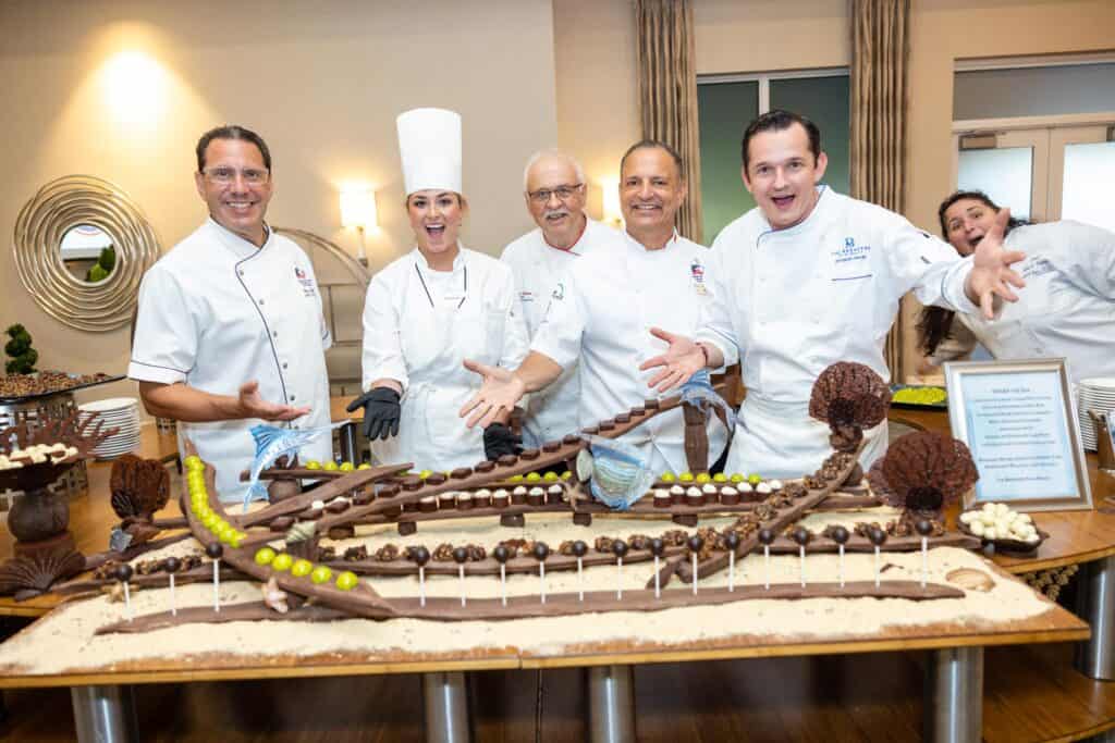 Celebrating culinary excellence with a team of chefs around a large, decorated chocolate cake.