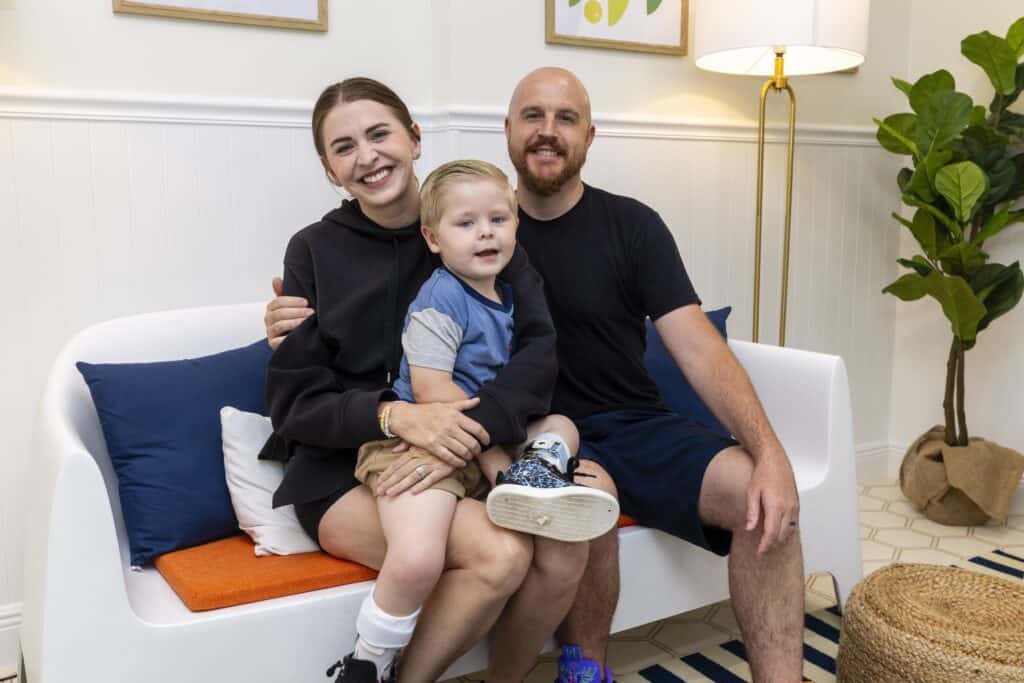 Family of three smiling on a white sofa in a cozy living room.