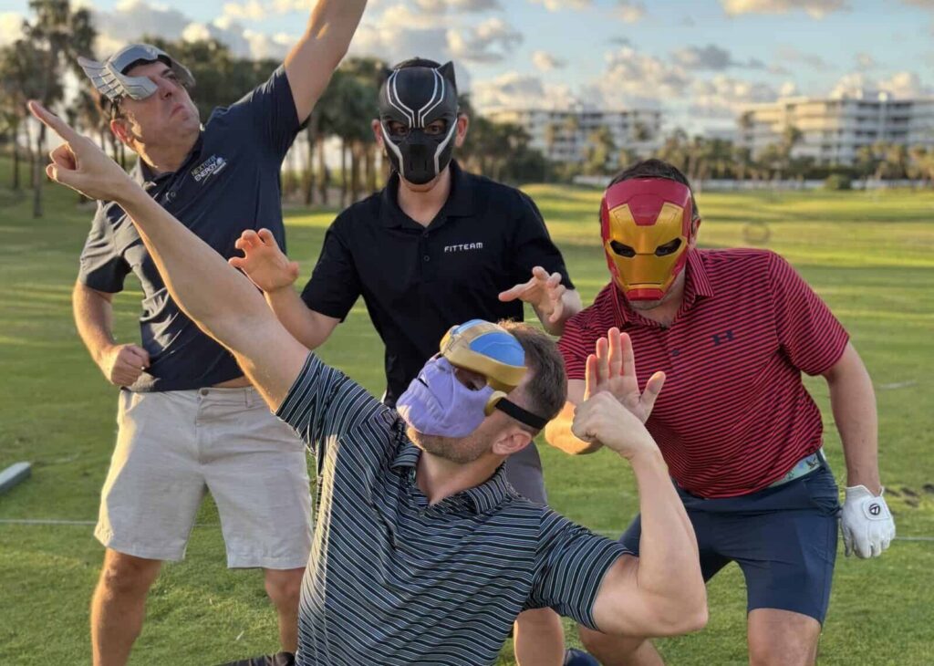 Group of people wearing masks playing golf outdoors on a sunny day.